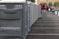 A line up of many grey portable toilets at a parking lot to be used by a crowd of people during an event or festival
