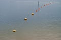 Line of yellow and orange buoys strung on rope stretched on surface of rippled water along the coast fencing the shallow water