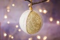 Linen and lace Christmas tree ball with ornament hanging on a branch. Golden garland glittering light in background. Greeting card