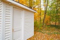 Lines of boards of white wooden building standing among trees in autumn colors and surrounded by leaf drop