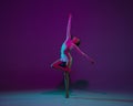 Young female athlete, rhythmic gymnastics artist on purple background with neon light. Beautiful girl practicing with Royalty Free Stock Photo