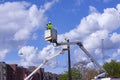 Lineworkers working on power lines in crane buckets high in the air from aerial lift. He is wearing yellow fluorescent clothes for