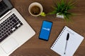 Linkedin app on phone screen. Workspace top view. Table desk with laptop, mobile phone, coffee, notepad, pen and plant.