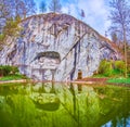Lion Monument carved in the rocky cliff of old sandstone quarry with a small pond and green park in front of it, Switzerland