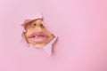 Lips of beautiful young woman visible through hole in pink teared paper Royalty Free Stock Photo