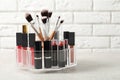 Lipstick holder with different makeup products on table against brick wall. Royalty Free Stock Photo