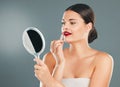 Lipstick, woman and mirror on studio background for beauty, fashion and aesthetics. Young model, red lips and makeup