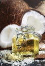 Liquid coconut oil in glass jar, broken coconuts, dark table, selective focus