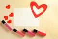 Liquid lipsticks with blank card and red hearts on color background