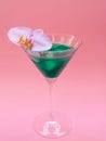 Liquid spirulina green drink with Phalaenopsis in cocktail glass on pink background.