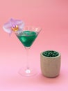 Liquid spirulina green drink with Phalaenopsis in cocktail glass and spirulina pills on pink background. Royalty Free Stock Photo