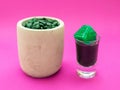 Liquid spirulina green drink in short cocktail glass and spirulina pills on pink background. Royalty Free Stock Photo