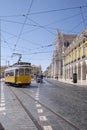 lisbon commerce square with a typical yellow streetcar and a blue tuc tuc, tourists in the background visiting the square in the