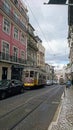 a typical Lisbon tram with cable on the street in the middle of the traffic with colorful buildings on the side under a