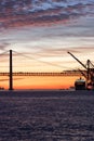 Lisbon 25th of April Bridge at sunset and industrial working cranes
