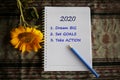 2020 new year resolutions list. Dream big. Set goals. Take action. With text on notebook paper, yellow flower and pen arrangement.