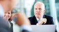 Listening critically to the proposal. Focused senior executive listening to his colleagues in a meeting while sitting Royalty Free Stock Photo