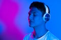 Listening to music. Asian man`s portrait on purple studio background in multicolored neon light. Concept of human emotions Royalty Free Stock Photo