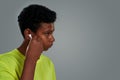 Listening to music. Side view of teenage african boy adjusting wireless earphones while standing against grey background