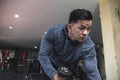A listless and seemingly unmotivated asian man makes dumbbell triceps kickbacks on a bench at a gym. Tricep and arm exercise and