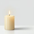 A lit beige cylindrical candle on a white surface against a light gray background. The Royalty Free Stock Photo