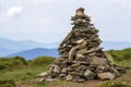 Lit by bright summer sun uneven mountain stones stacked and balanced like pyramid pile on green grassy valley on light white blue