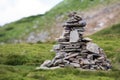 Lit by bright summer sun uneven mountain stones stacked and balanced like pyramid pile on green grassy valley on light white blue