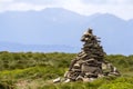 Lit by bright summer sun uneven mountain stones stacked and balanced like pyramid pile on green grassy valley on light white blue