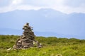 Lit by bright summer sun uneven mountain stones stacked and balanced like pyramid pile on green grassy valley on light white blue