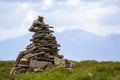 Lit by bright summer sun uneven mountain stones stacked and balanced like pyramid pile on green grassy valley on light white blue