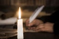 A lit candle against the background of blurred scrolls, writer`s hand, books and bird`s feather