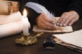 A lit candle against the background of blurred scrolls, writer`s hand, books and bird`s feather