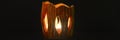 The lit candle burns inside the candlestick on a black background. beautiful fire light from the slits of a candleholder made of c