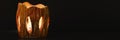 the lit candle burns inside the candlestick on a black background. beautiful fire light from the slits of a candleholder made of c