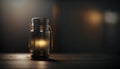 a lit candle in a glass jar on a wooden table in a dark room with light coming from the top of the jar and the bottle. Royalty Free Stock Photo