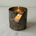 A lit candle is housed in a metal holder with a unique, patchwork-like design featuring Royalty Free Stock Photo