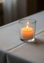A lit candle is placed in a clear glass holder on a white tablecloth-covered surface. Royalty Free Stock Photo