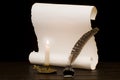 A lit candle and quill with inkwell against a background of a scroll of parchment