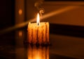 A lit candle on a reflective surface creates a warm glow. The short candle features melted wax Royalty Free Stock Photo