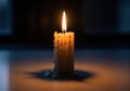 A lit candle sits on a reflective surface in a dimly lit environment. The candle is partially Royalty Free Stock Photo