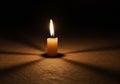 A lit candle stands on a textured surface, casting a warm glow in an otherwise dark Royalty Free Stock Photo