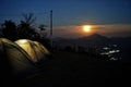 Lit-up camps on a campground with a rising full moon on a hill top in the background. Trekking and camping in the Himalayas.