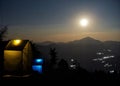 Lit-up camps on a campground with a rising full moon on a hill top in the background. Trekking and camping in the Himalayas.