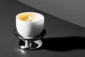 Lit white candle in modern holder on gray surface casting shadow Royalty Free Stock Photo