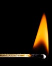 A lit wooden match burns with an orange flame against a black Royalty Free Stock Photo