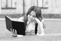 Literature for kids. Lesson on fresh air. Cute small child reading book outdoors. Schoolgirl school uniform laying on Royalty Free Stock Photo