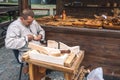 Lithuanian craftsman in traditional costumes carving wood and selling his handmade wooden artifacts