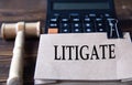 LITIGATE - word on light brown paper against the background of a calculator and a judge\'s gavel