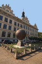 Unusual monument in the form of a metal ball with embossed pictures. Beautiful ancient building at the background