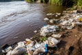 littering and urban pollution of river bank with plastic bags, bottles, and packaging